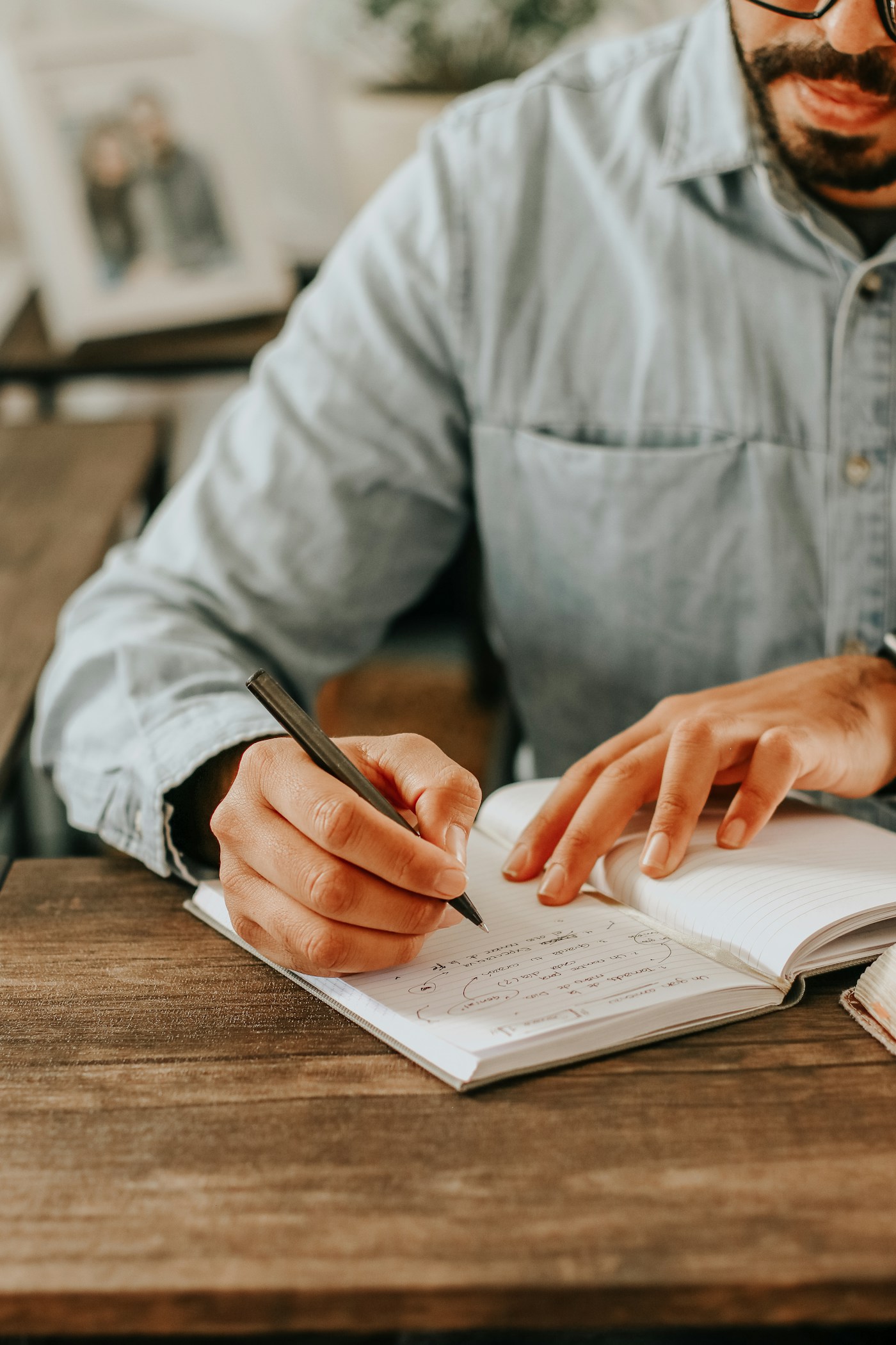 Mãos escrevendo em um caderno aberto sobre uma mesa